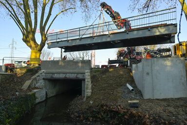 Grue de chantier soulevant la passerelle métallique au-dessus de la Romagne